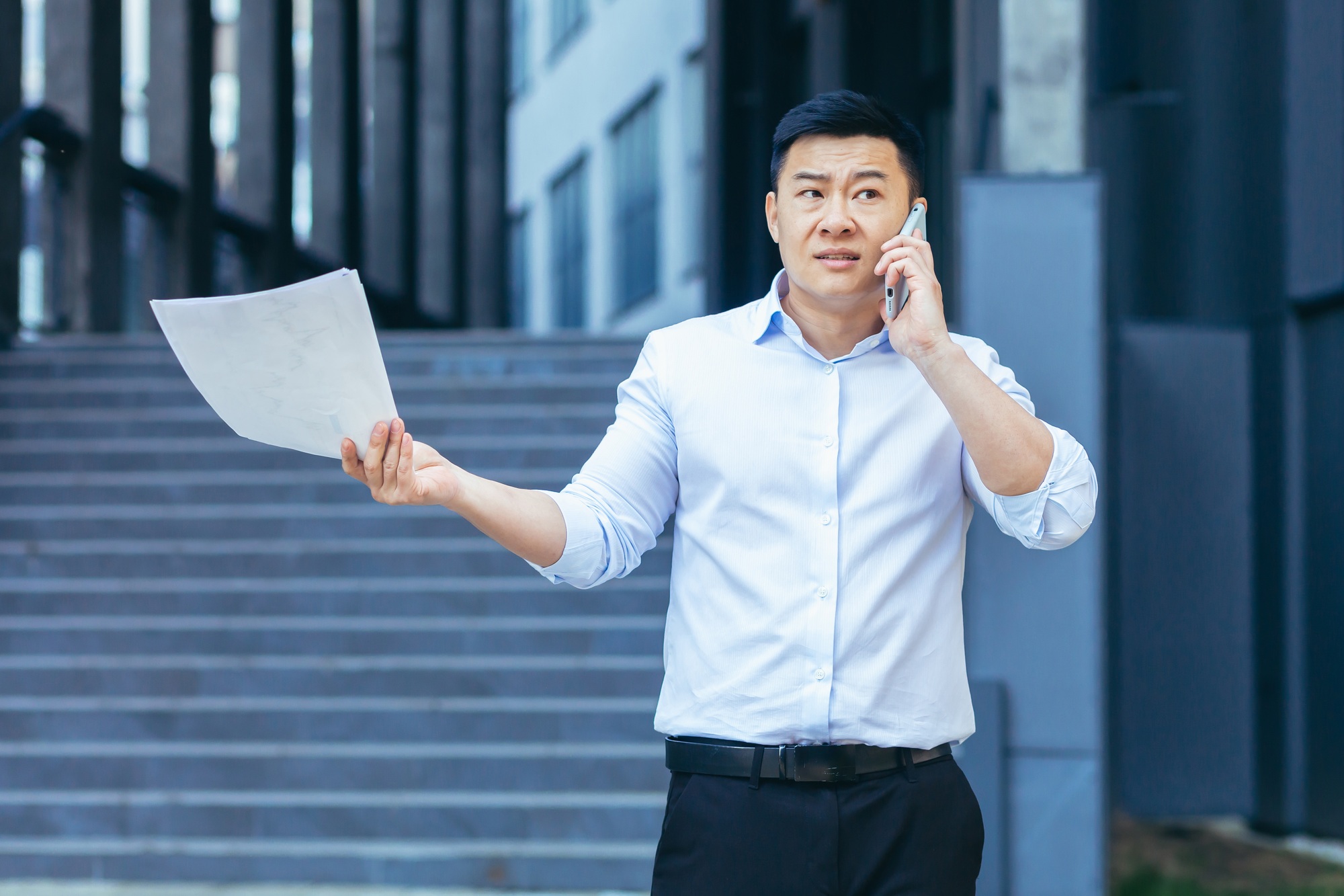 Frustrated insurance agent with documents talking on the phone outside the office