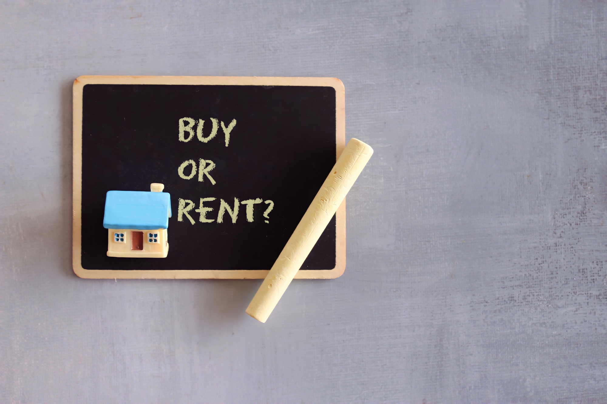 Top view of chalkboard with text BUY OR RENT, toy house and chalk